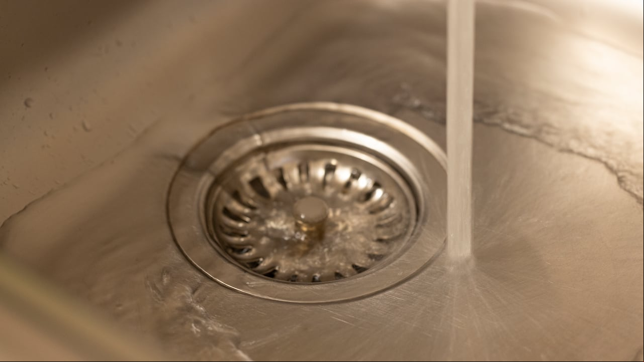Primer plano de un orificio de desagüe de un lavaplatos de cocina con agua saliendo.