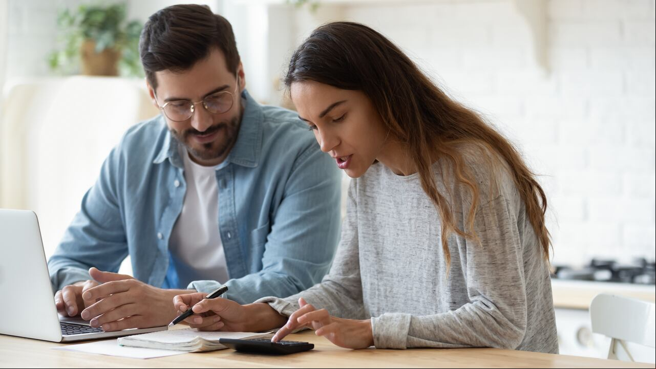 Joven esposo y esposa usando calculadora computadora portátil istrar finanzas calcular facturas hablar de impuestos hacer papeleo juntos sentarse en casa mesa discutir presupuesto de planificación de pago de dinero de préstamo hipotecario familiar