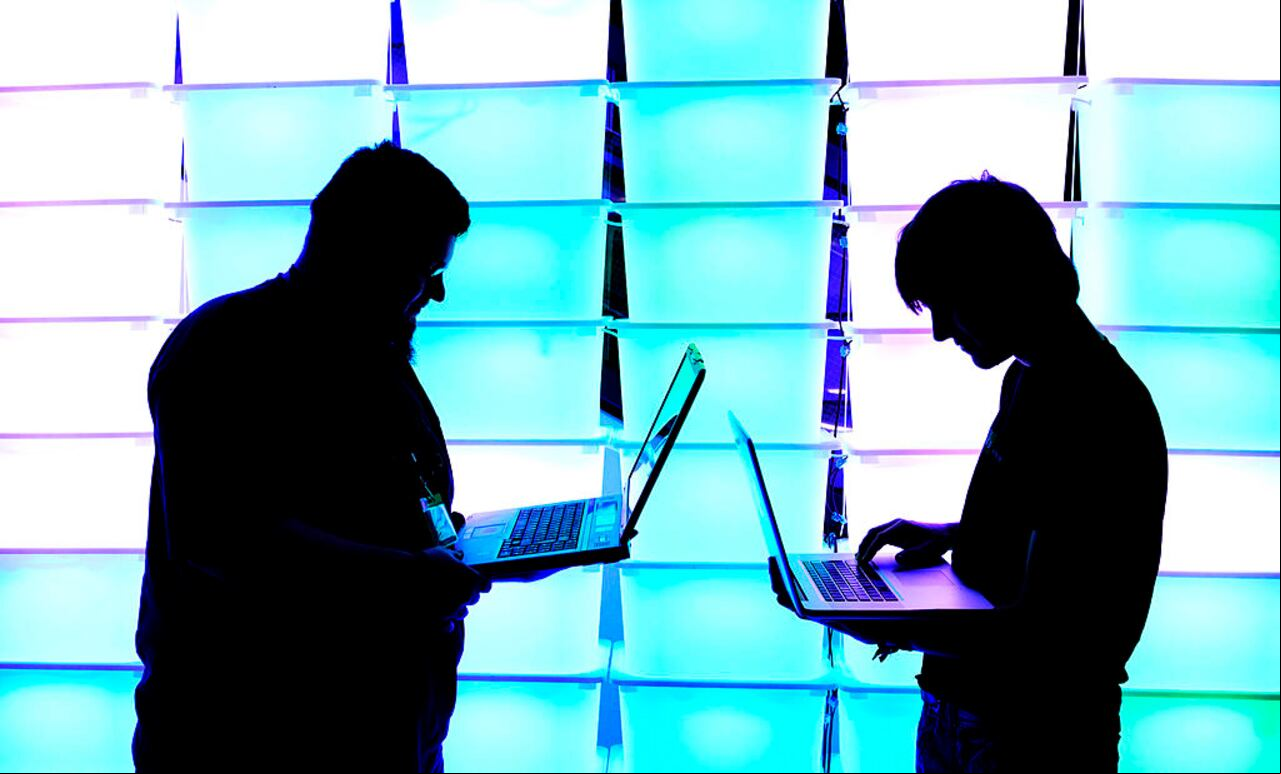 Los participantes sostienen sus computadoras portátiles frente a una pared iluminada en el congreso anual de piratas informáticos Chaos Computer Club (CCC), llamado 29C3, el 28 de diciembre de 2012 en Hamburgo, Alemania (Foto de Patrick Lux/Getty Images)