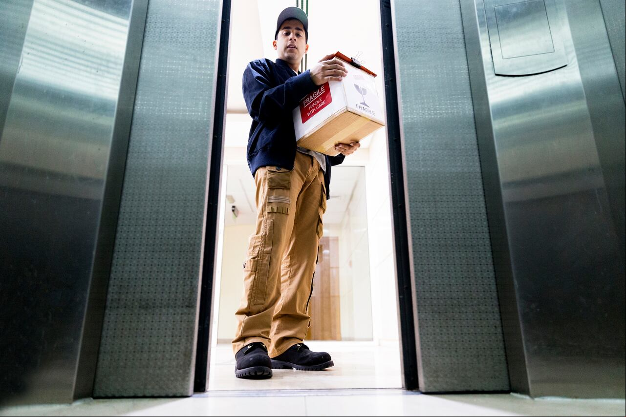 Young delivery man holding the delivery packaging and entering a building elevator