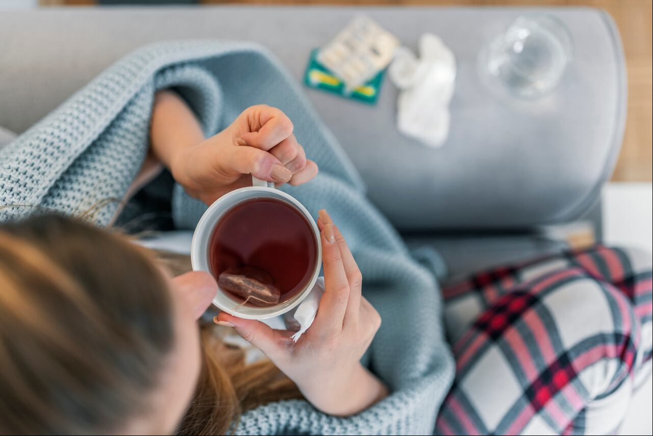 Vista superior de una mujer enferma con dolor de cabeza sentada en un sofá en casa envuelta en una manta durante el día. Enfermedad, concepto de problema de virus estacional. Mujer enferma con gripe acostada en el sofá.