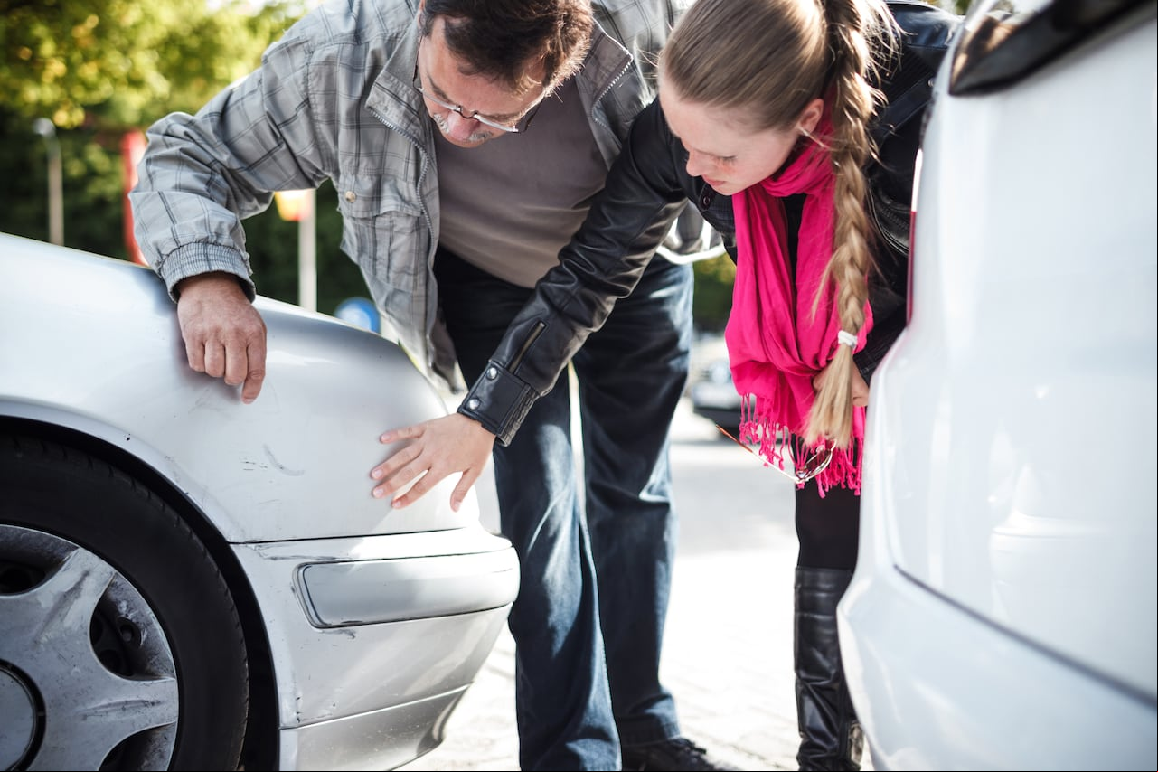 Close-up of man and younger woman examining car after accident.