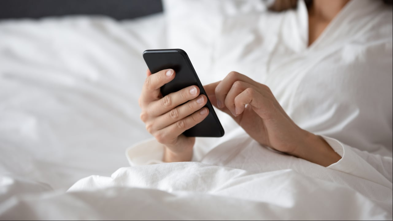 La mujer se despertó acostada en la cama debajo de la manta, use el teléfono para aprender una nueva aplicación, planifique el día, verifique la lista de tareas diarias del calendario personal, busque información, revise los mensajes del buzón de correo electrónico, comience el día con el concepto de gadget