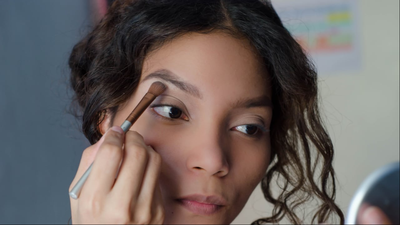 Mujer hermosa joven aplicando sombra de ojos con una brocha de maquillaje en el hueso de la frente