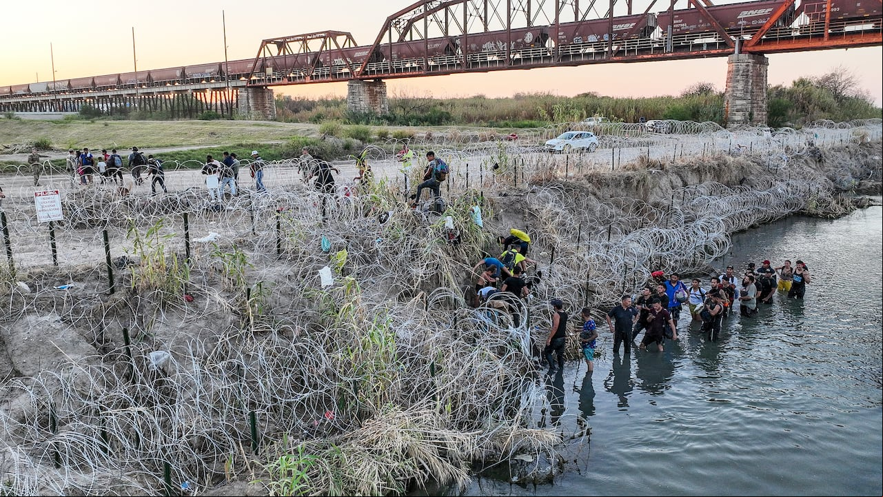 Las personas que cruzaron la frontera entre Estados Unidos y México buscan un paso a través de alambre de púas en el lado texano del Río Grande.