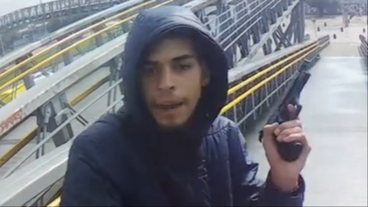 El antisocial, portando una chaqueta color azul oscuro y con capucha, ingresa corriendo al punto, con un arma de fuego en una mano y señala la patineta eléctrica con la otra. Después se apodera de este vehículo.